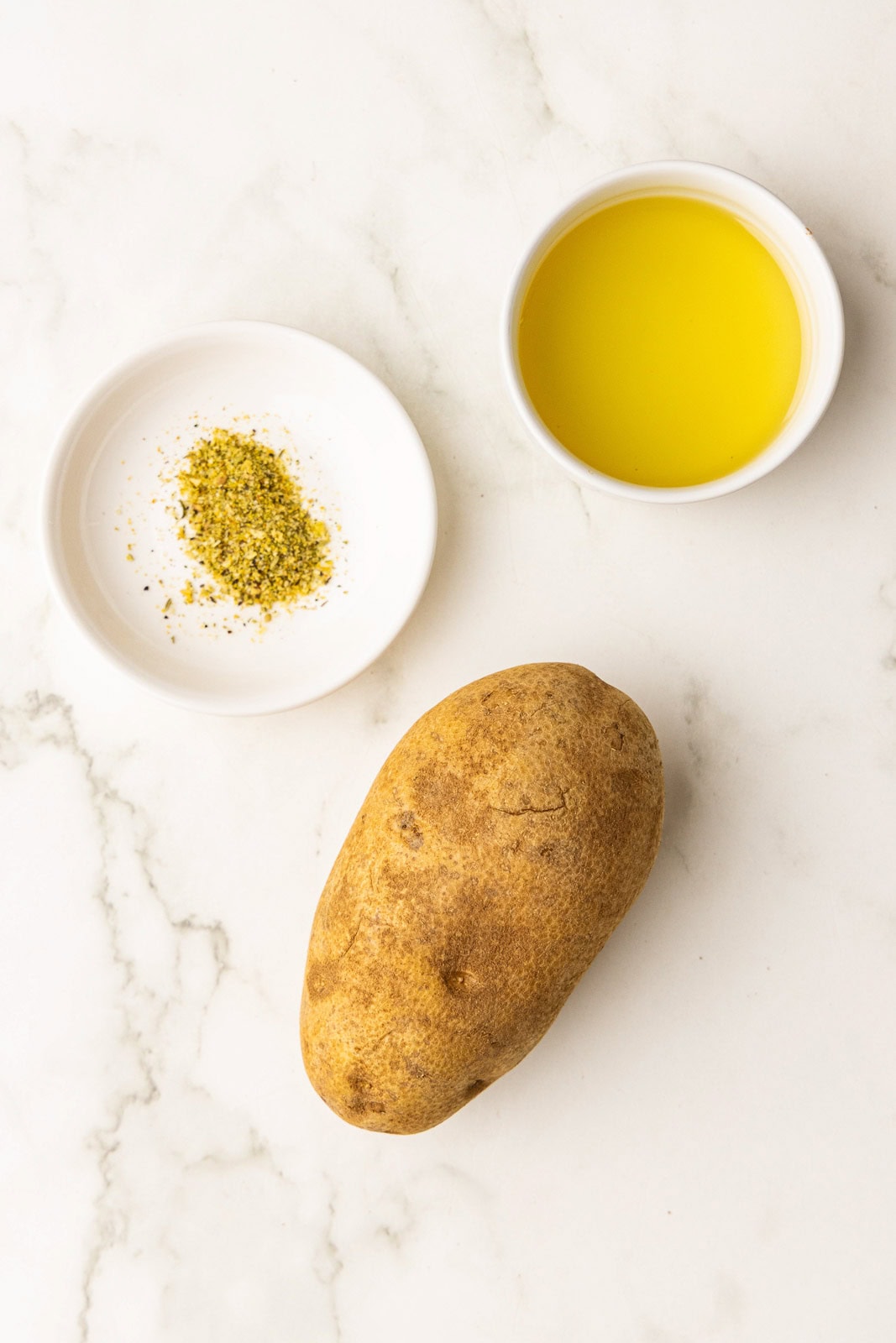 ingredients to include russet potato, small white bowls of avocado oil and seasoning