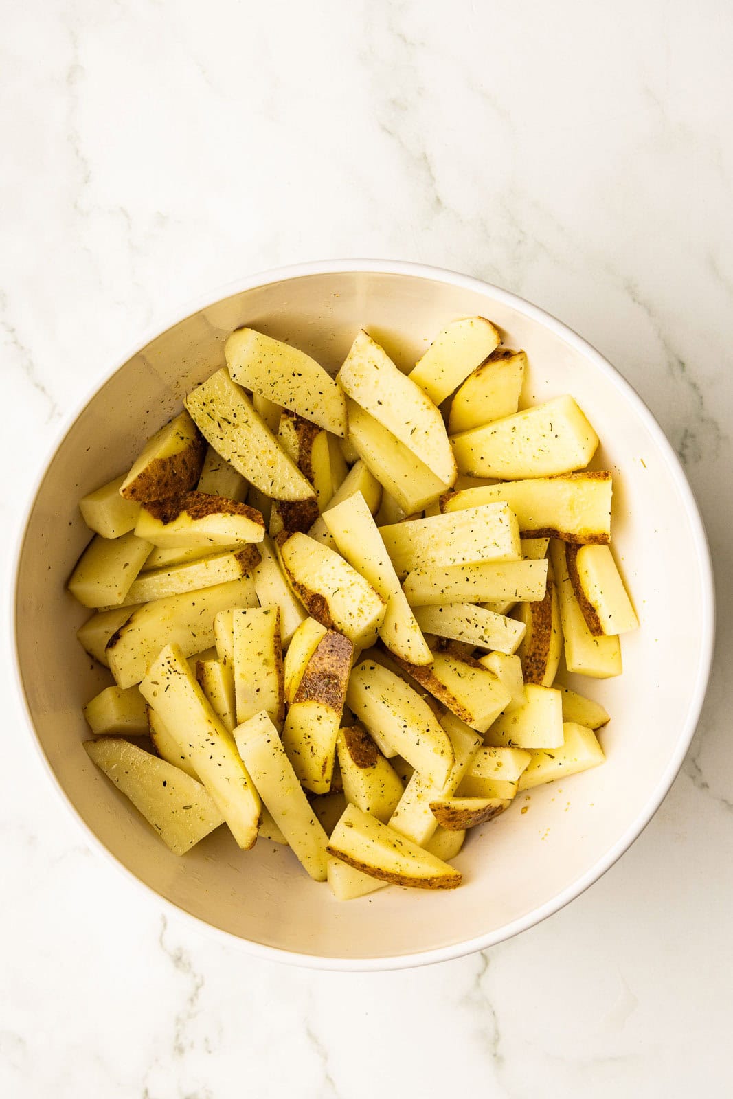 large white bowl containing sliced oiled and seasoned potatoes