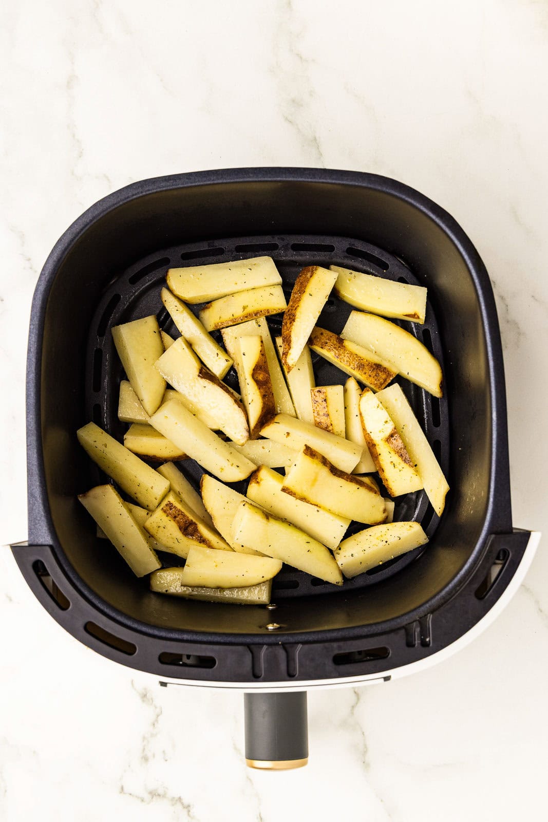 overhead view of black air fryer containing seasoned potato slices