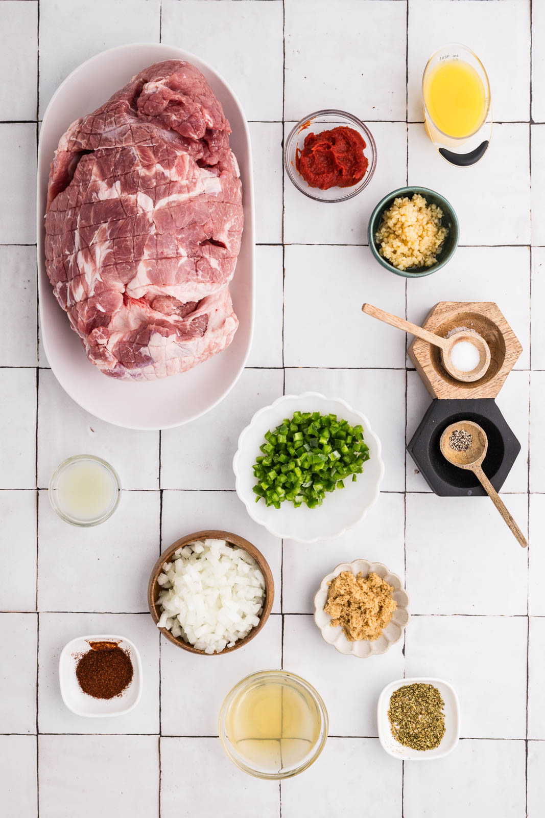 ingredient for IP Carnitas to include large white platter with pork shoulder, small bowels filled with tomato paste, chicken broth, minced garlic, jalapeno pepper, diced onion, brown sugar, salt, pepper, orange juice, lime juice, oregano and chili powder