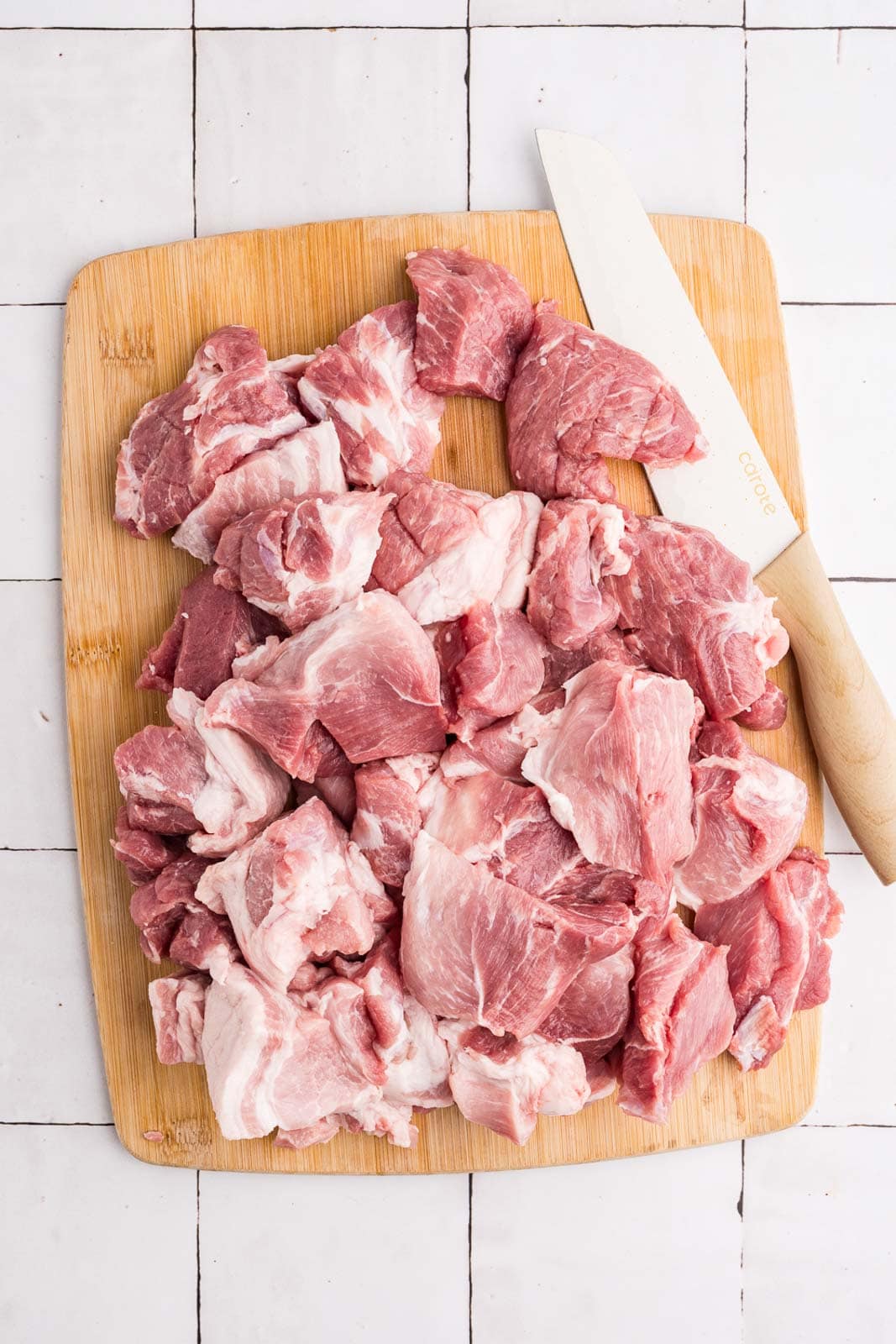 wooden cutting board with knife and cubed pork shoulder