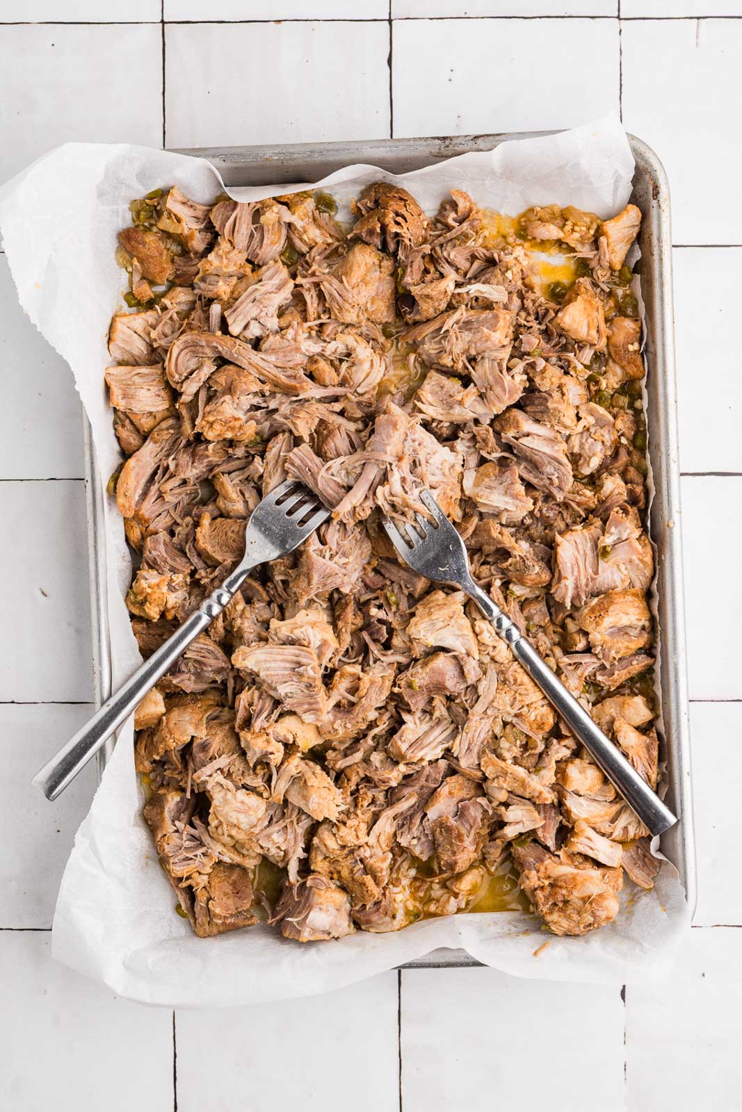 sheet pan lined with parchment paper with shredded pork and to forks