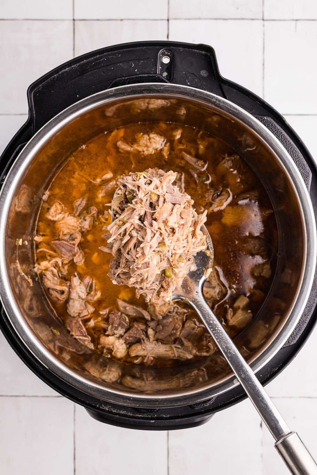 overhead view of instant pot with cooked pork and large ladle over instant pot with pork