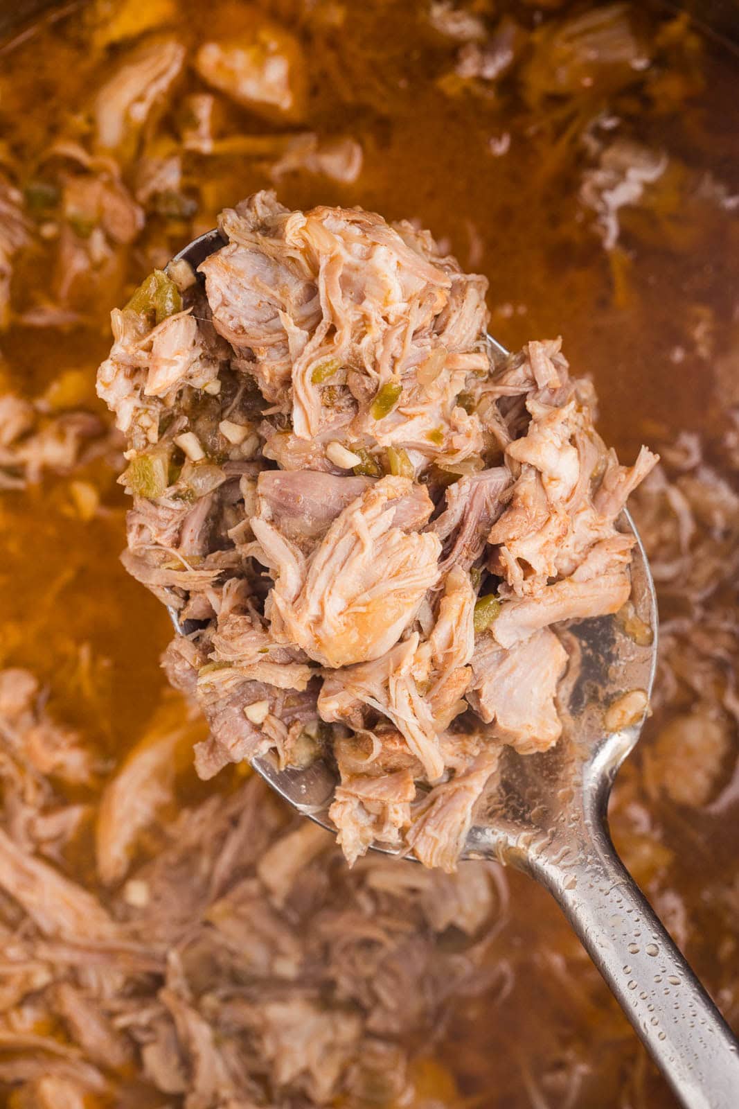 closeup view of ladle of cooked pork with instant pot filled with pork in background