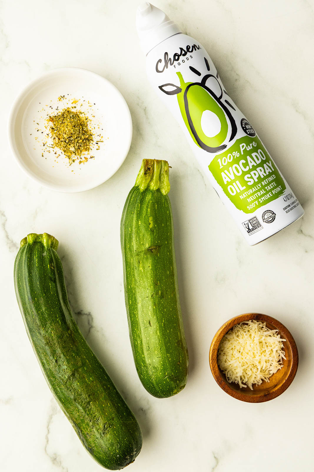 ingredients to include 2 avocados, can of avocado spray, small white bowl of seasoning and small wooden bowl of Parmesan cheese