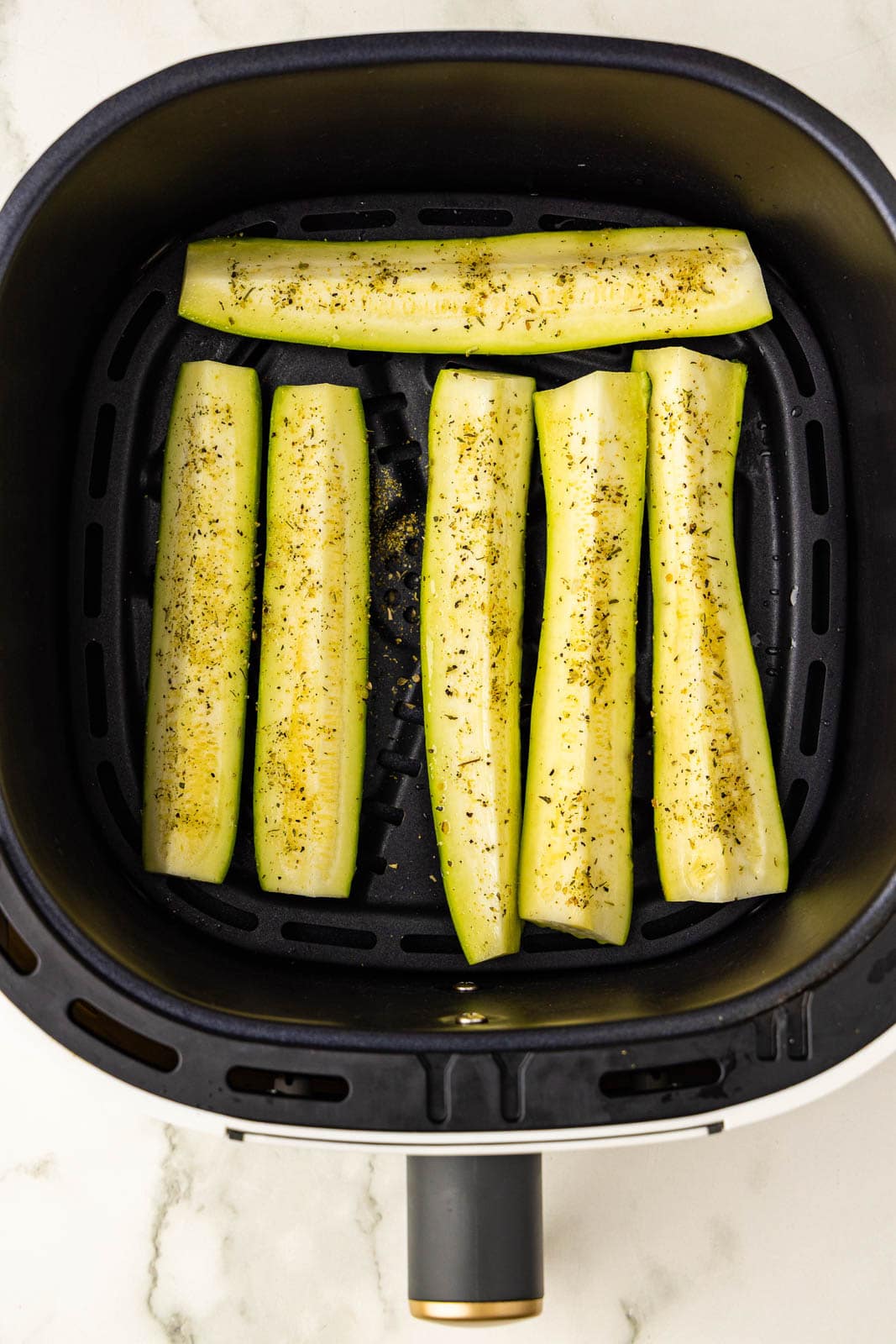 overhead view of black air fryer containing 6 seasoned zucchini slices