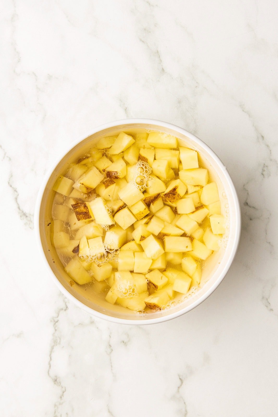 white bowl of diced potatoes in water