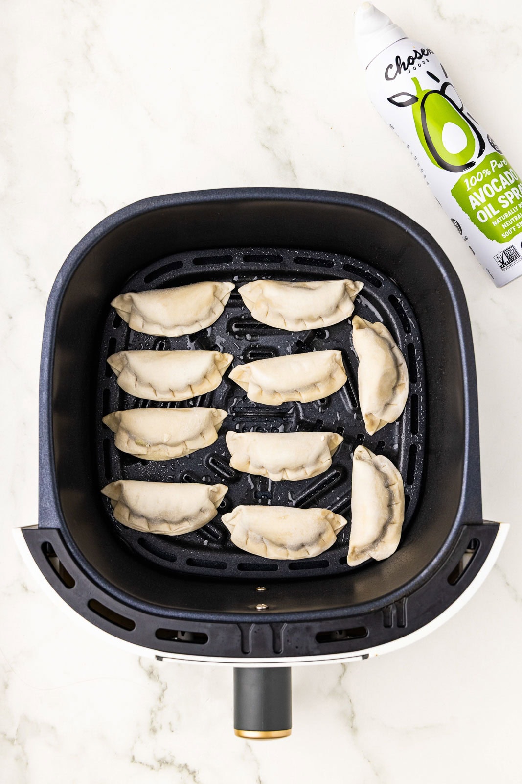 overhead view of black air fryer with 10 frozen pot stickers with can of avocado spray on side