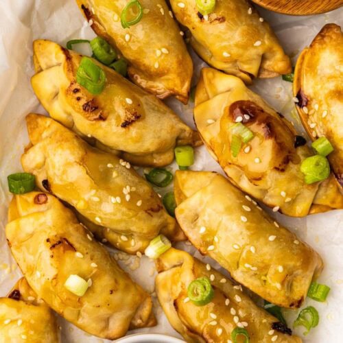 closeup of 10 air fried pot stickers sprinkled with sesame seeds with white bowl of dipping sauce and one bowl of sesame seeds