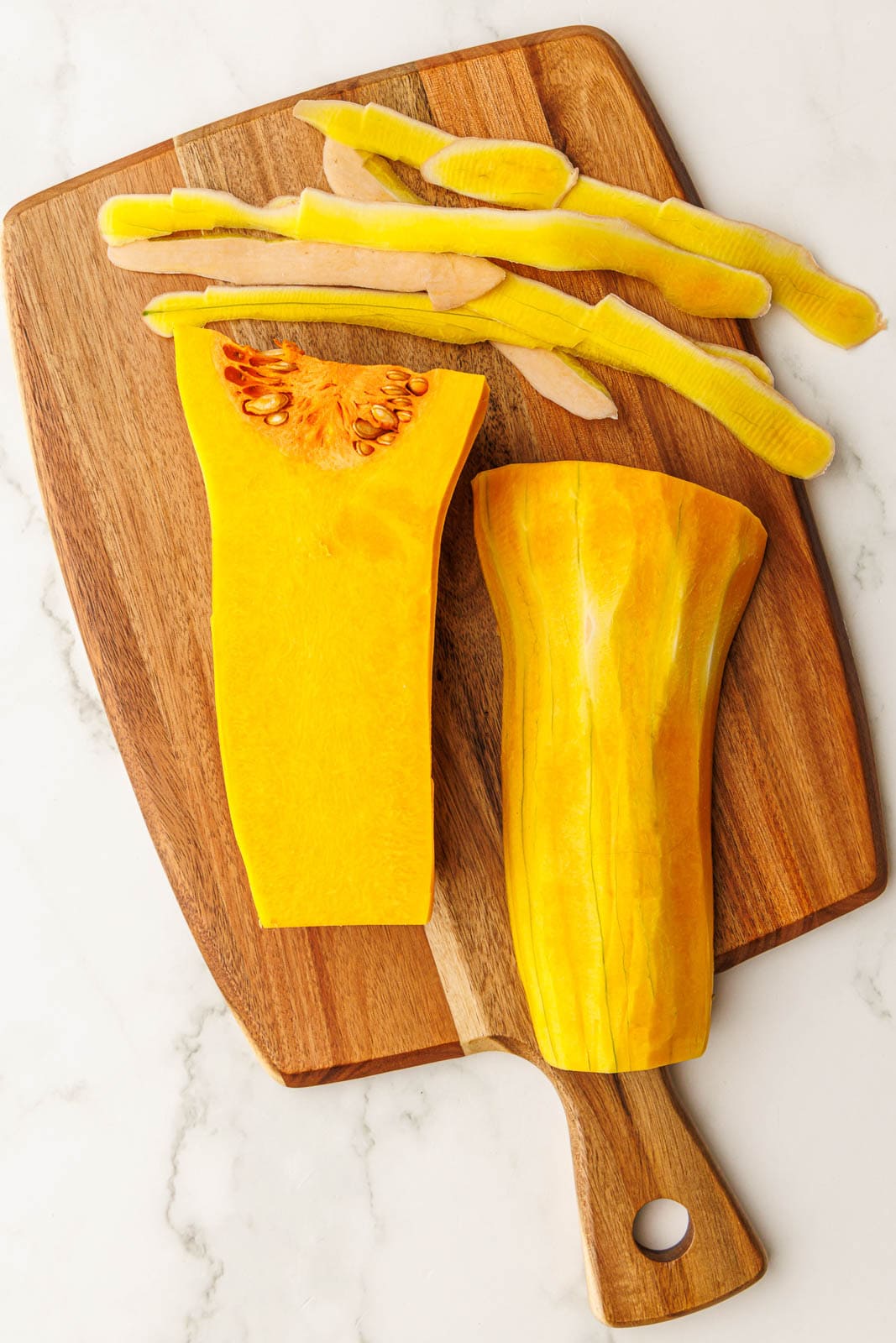 wooden cutting board with halved and peeled butternut squash