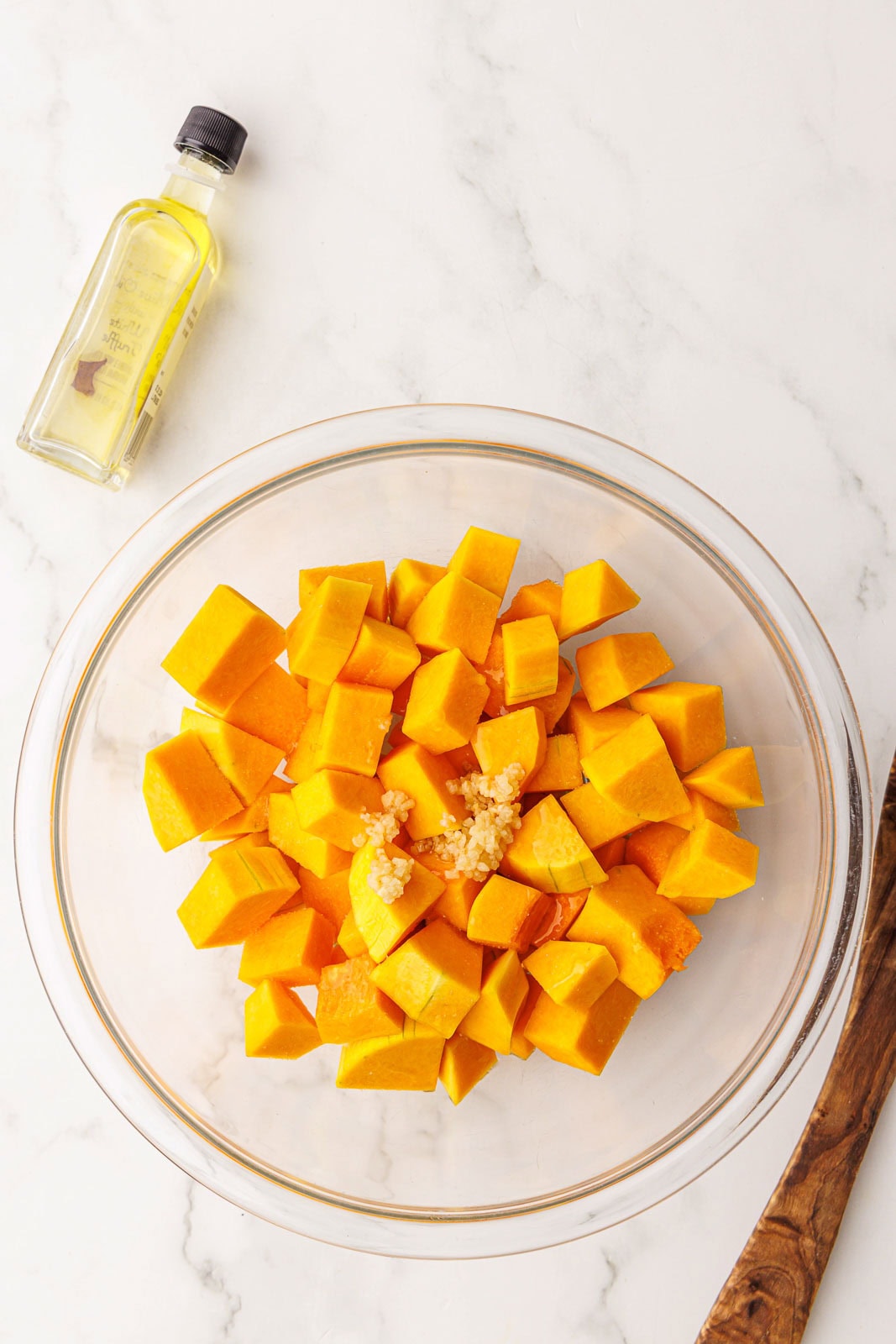 overhead view of glass bowl of butternut squash and garlic with bottle of olive oil on side