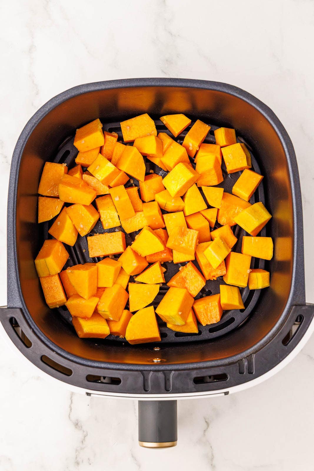 overhead view of black air fryer containing prepared butternut squash
