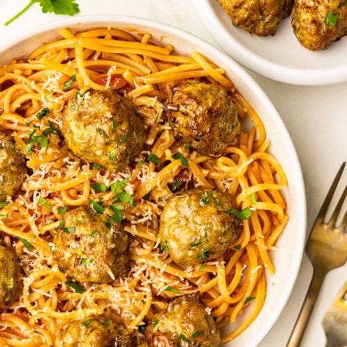 overhead view of white plate of pasta and turkey meatballs, with 2 forks and platter of turkey meatballs on side