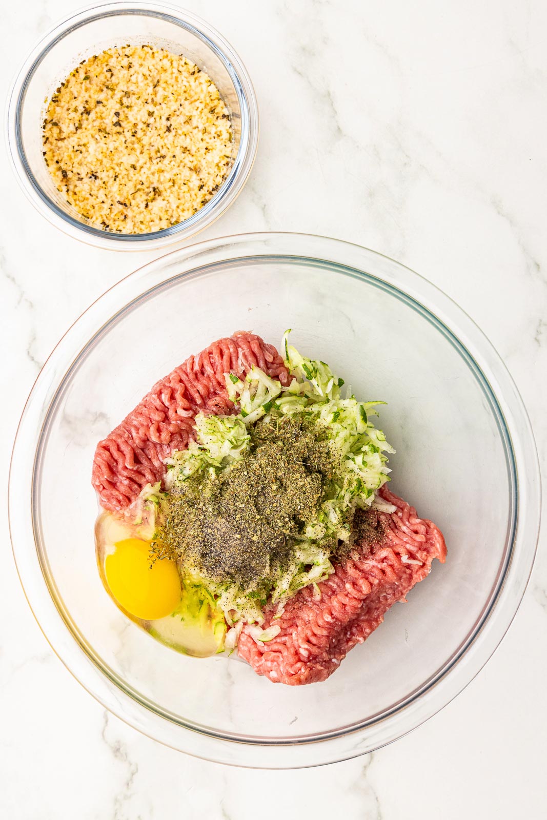 glass bowl of turkey, egg, zucchini, salt and pepper and seasoning, with small bowl of panko breadcrumbs mixture on side