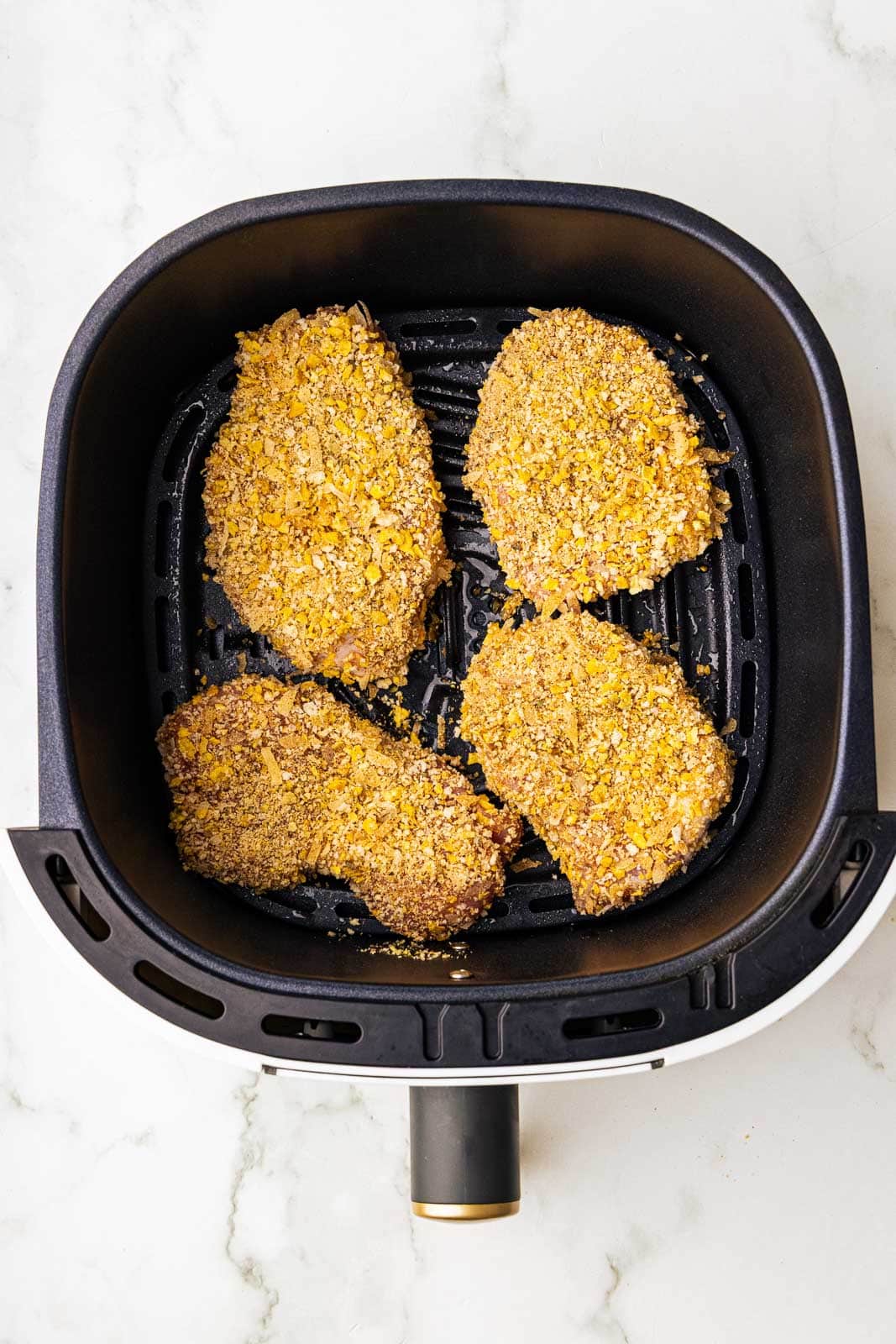 black air fryer with four coated pork chops