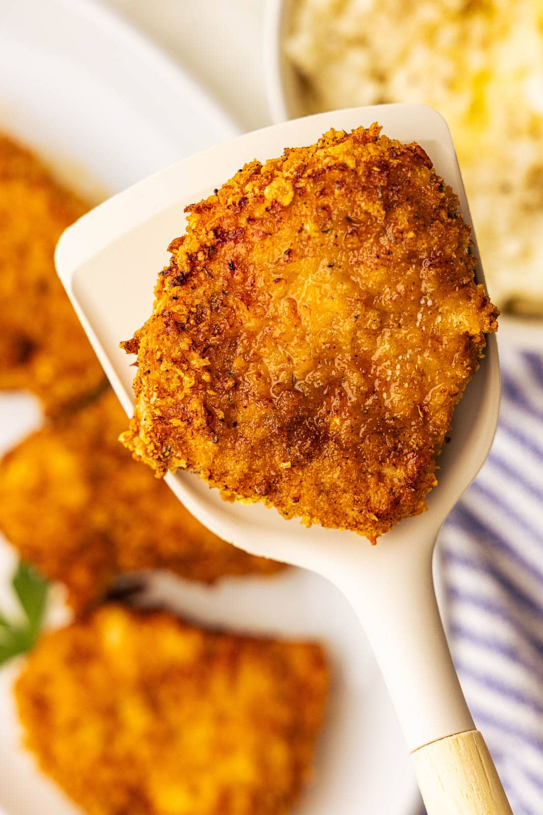 closeup of spatula holding air fried pork chop with platter of pork chops in background