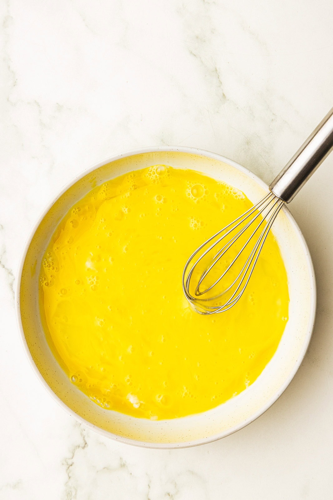 white bowl with beaten eggs and wire whisk