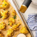 overhead view of parchment lined cooking sheet containing air fried cauliflower and Sriracha ranch dip, with white air fryer in background