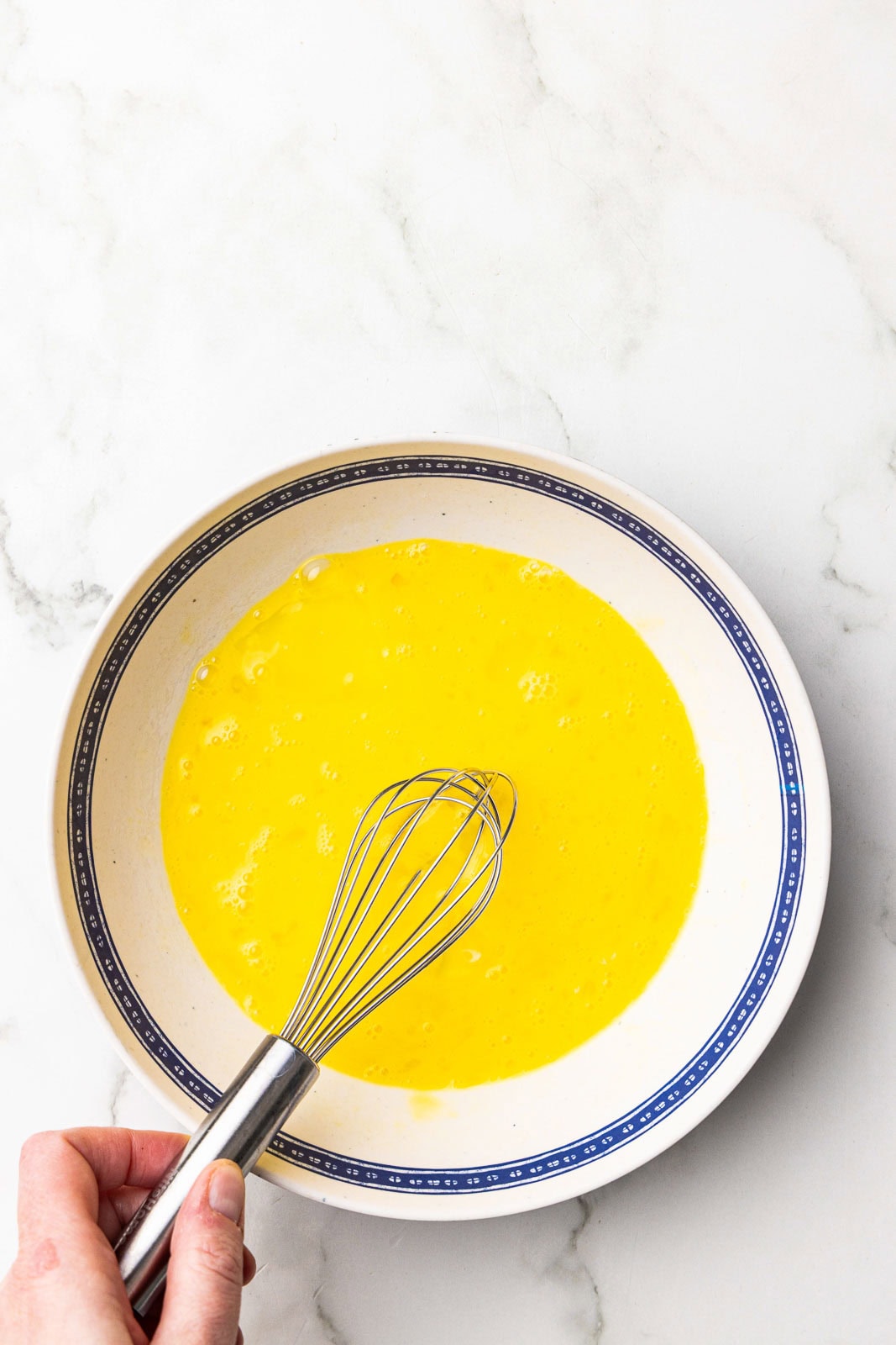 blue rimmed white bowl of eggs with whisk inserted