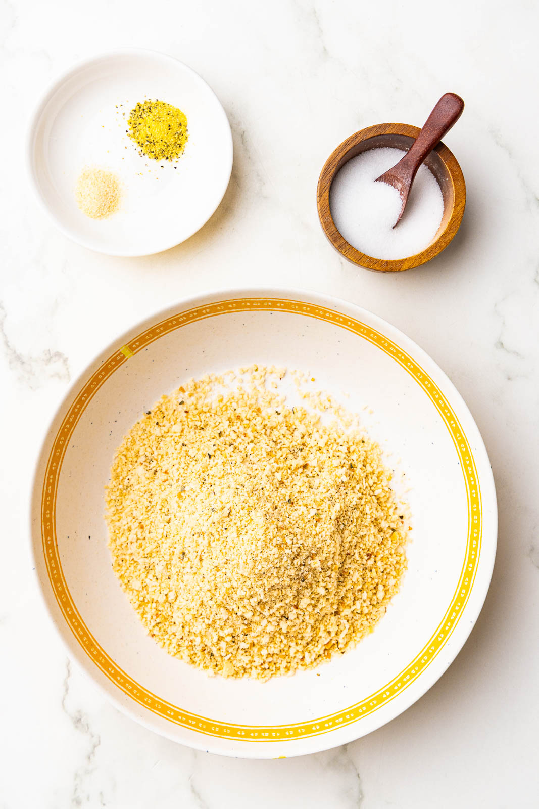 yellow rimmed white bowl of panko breadcrumbs, surrounded by bowls of salt, lemon pepper seasoning and garlic powder