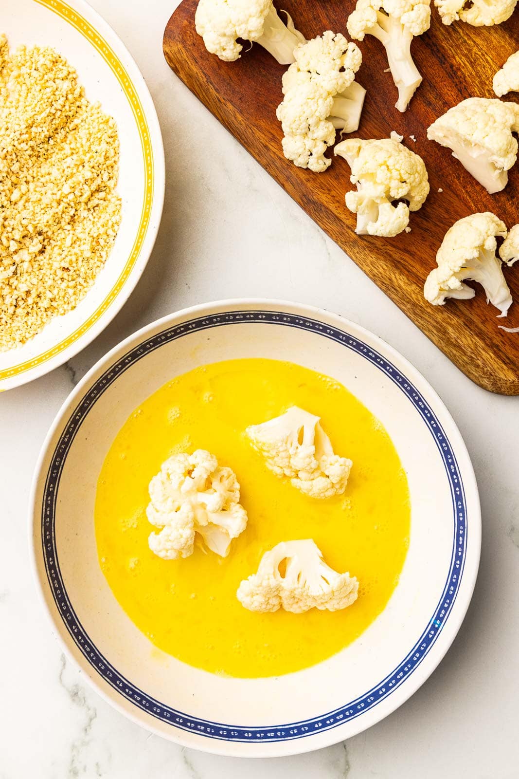 bowls of egg mixture with florets, panko breadcrumbs and cutting board with florets
