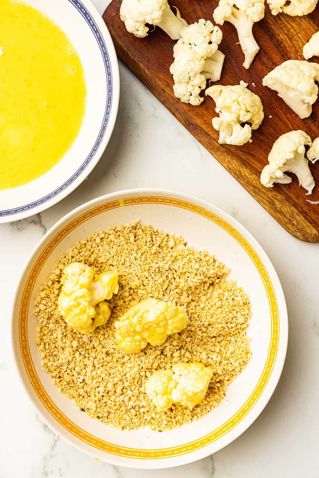bowls of panko breadcrumbs with florets, egg mixture, and cutting board with florets
