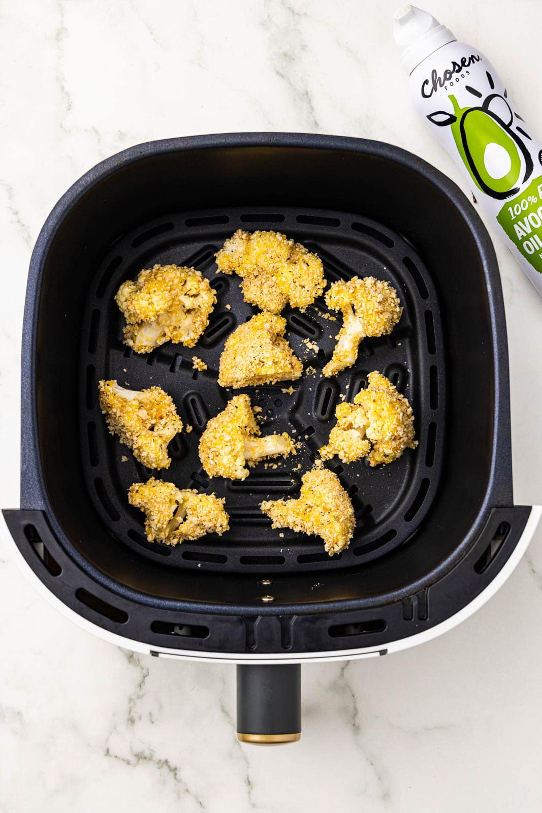 overhead view of black air fryer with florets and avocado oil spray on side
