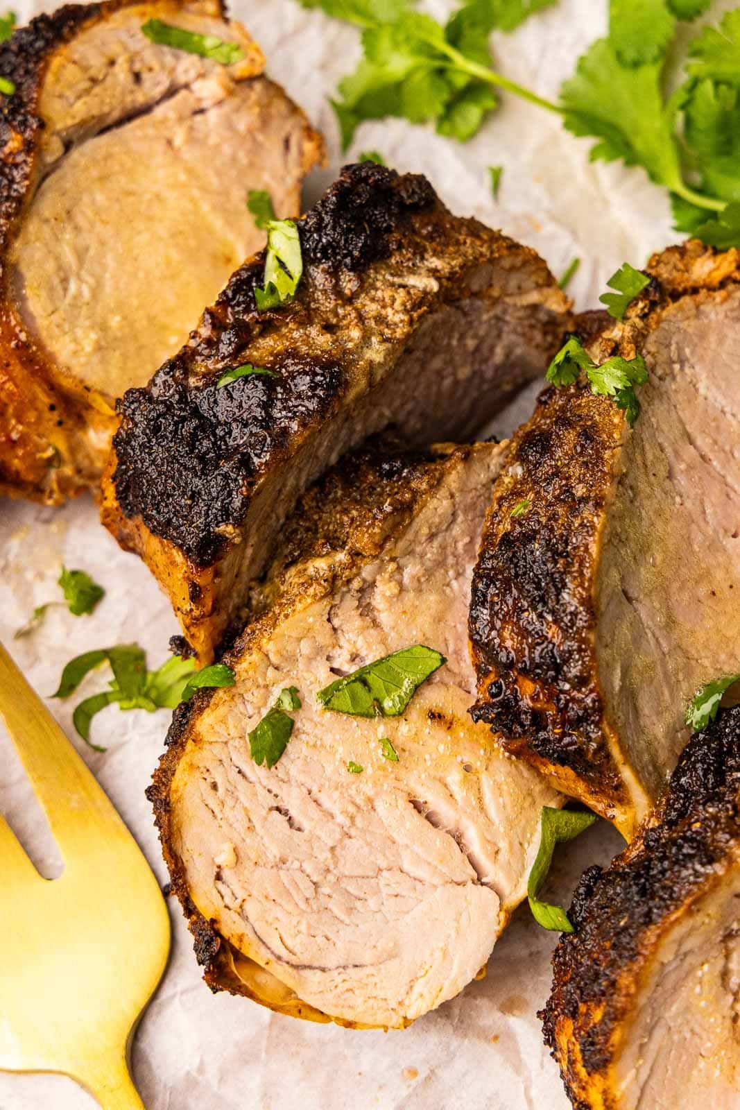 closeup of sliced pork tenderloin with gold fork on parchment paper
