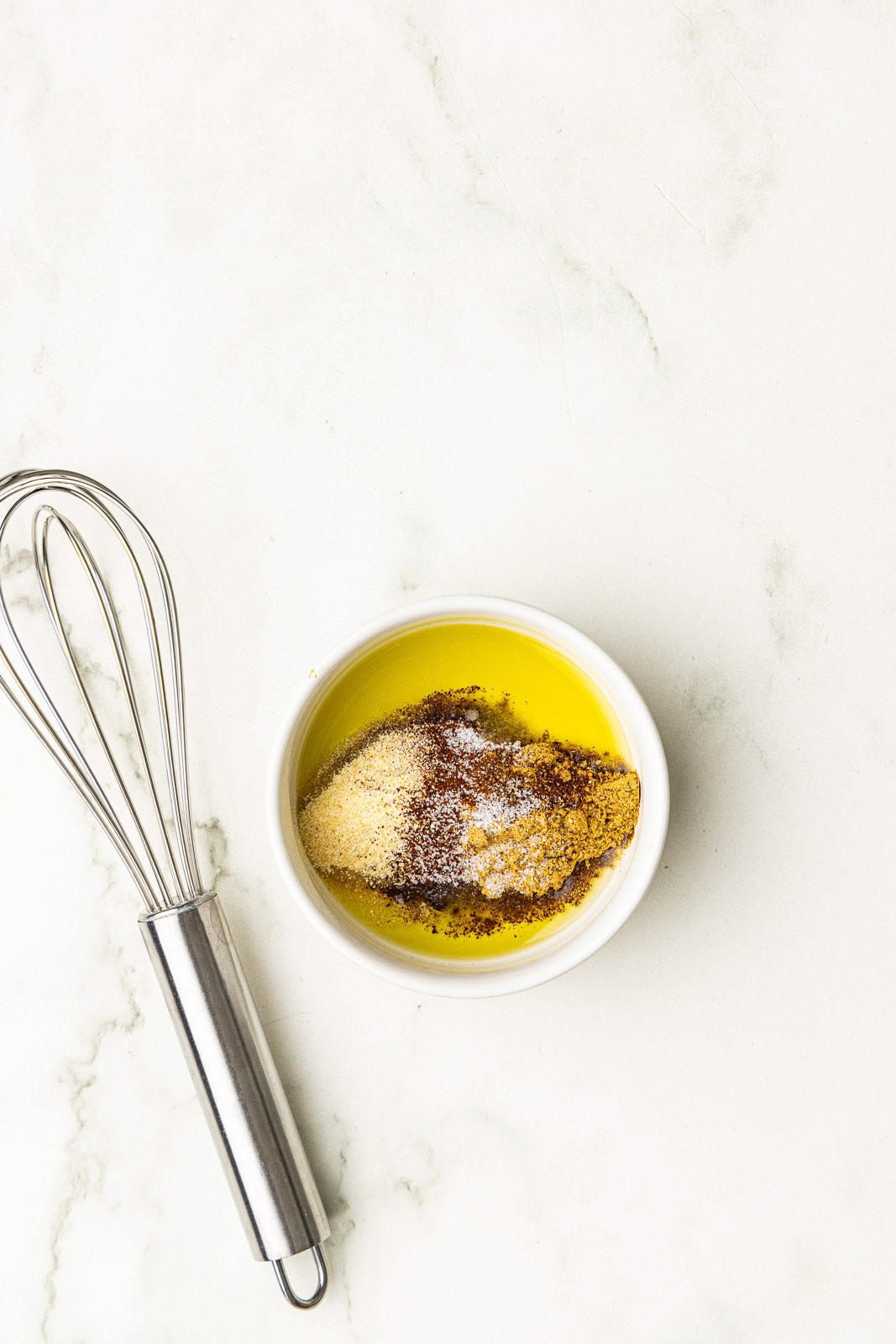 bowl of seasonings and olive oil with whisk on side