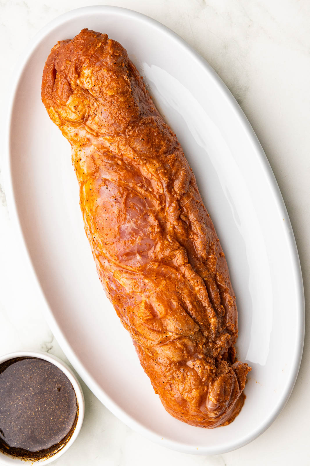 white platter with pork tenderloin and bowl of seasoning mix on side