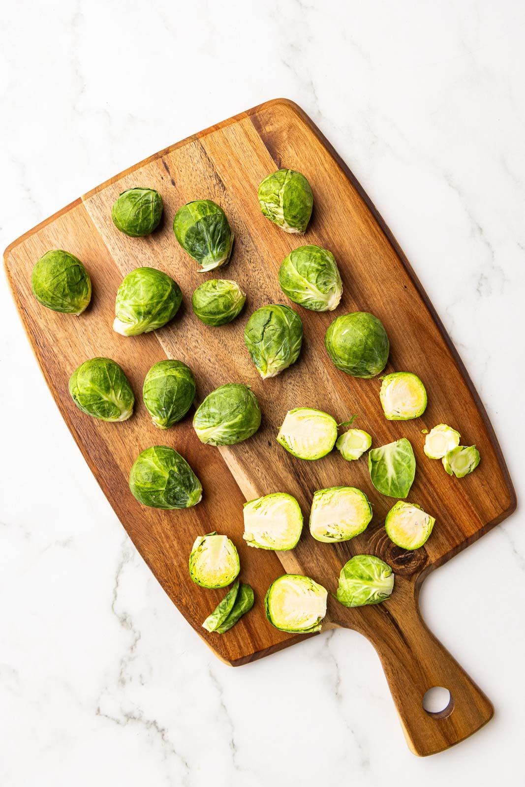 wooden cutting board with Brussels sprouts, some halved and trimmed