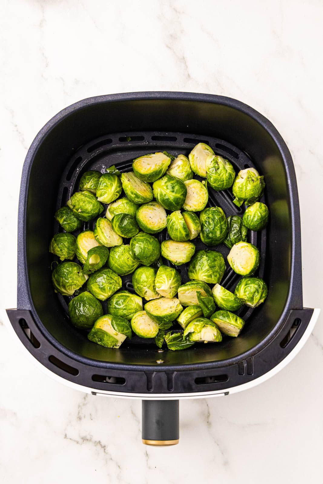 overhead view of black air fryer containing uncooked Brussels sprouts