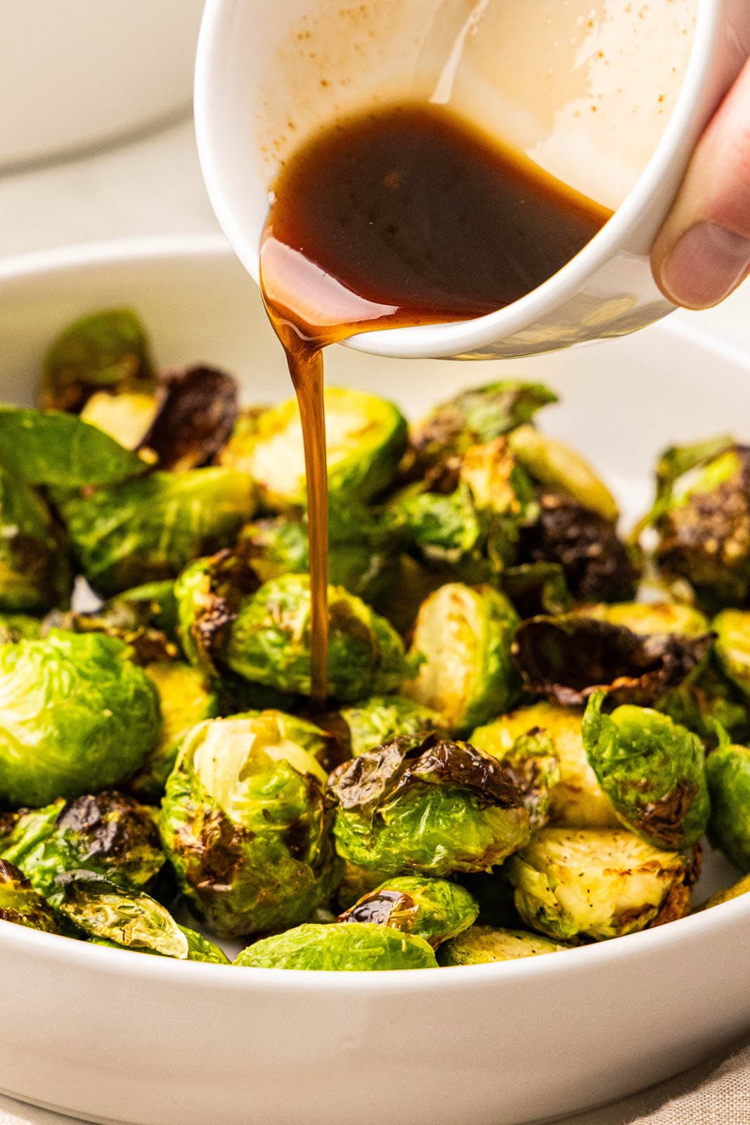 closeup of white bowl of Brussels sprouts with bowl of glaze being poured over it