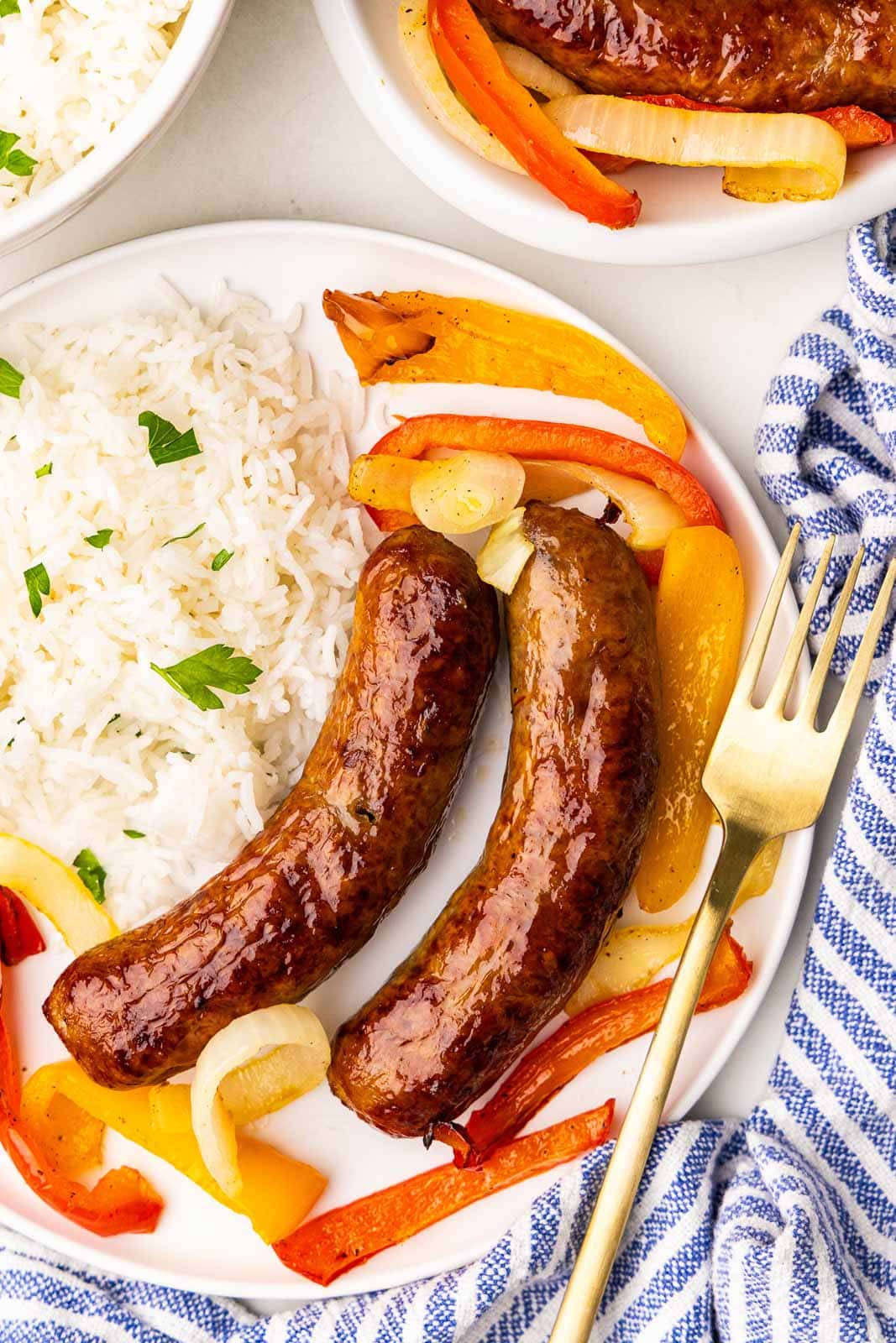 overhead view of white plate with 2 sausage, rice and peppers with gold fork on side