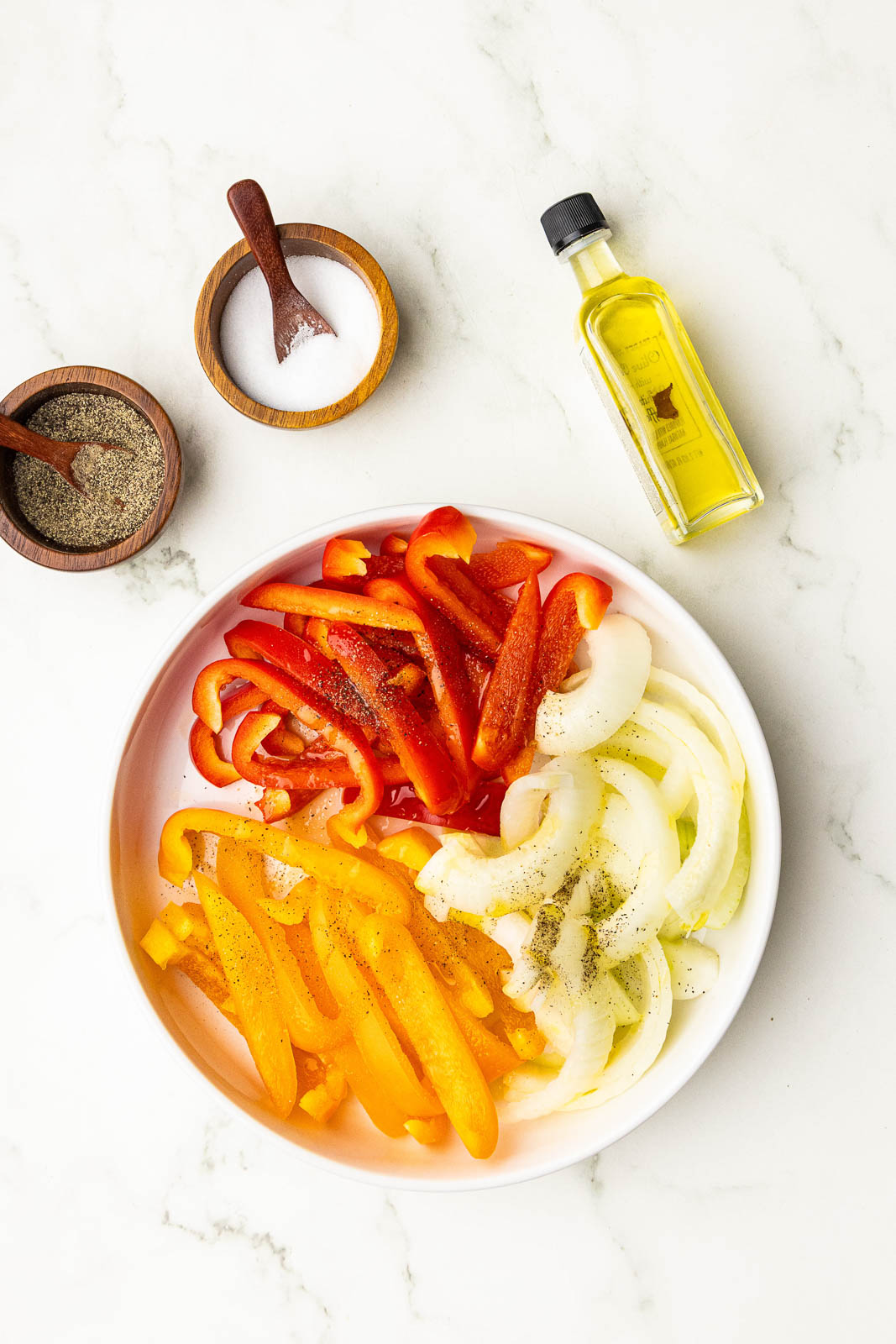 white plate of peppers and onions surrounded by salt and pepper bowls and olive oil
