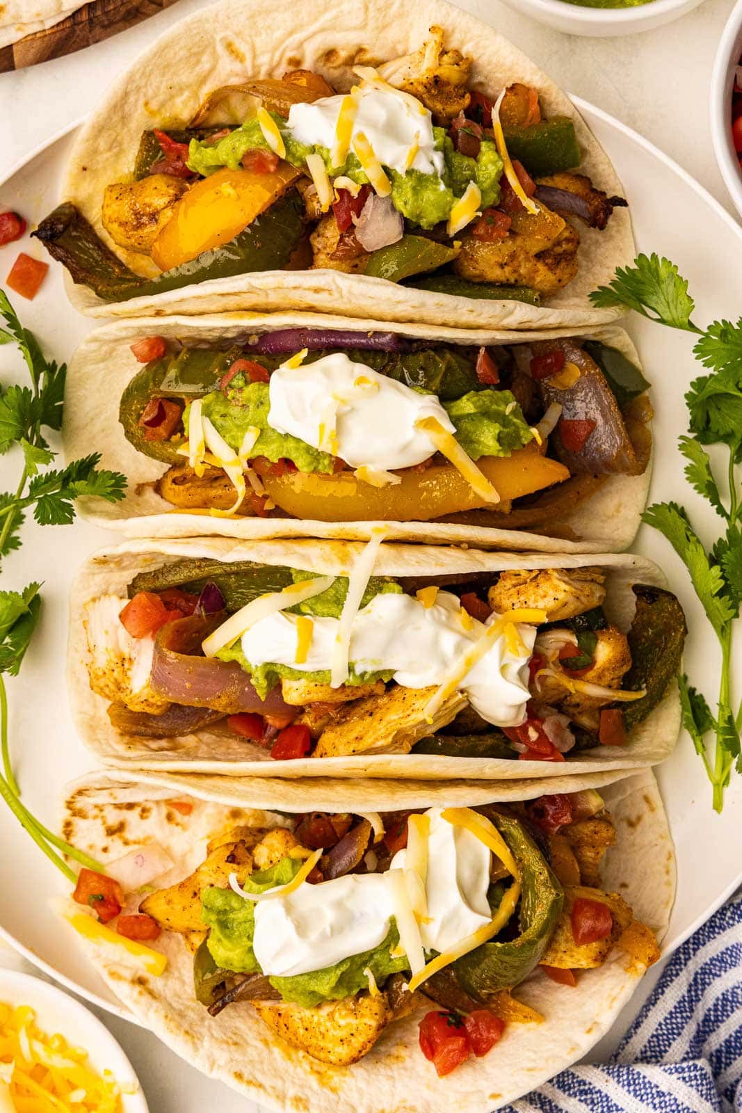 overhead view of four prepared fajita mixture in soft tortillas on a white platter