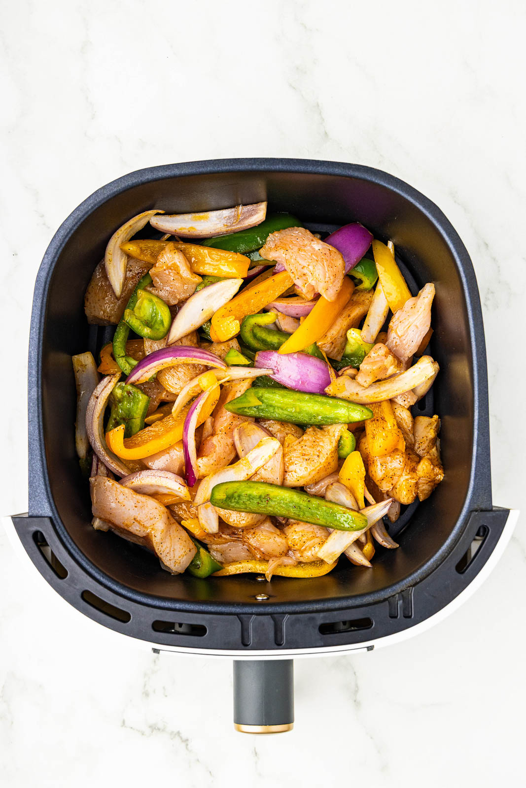 overhead view of black air fryer containing seasoned fajita mixture of chicken breasts, peppers and onions