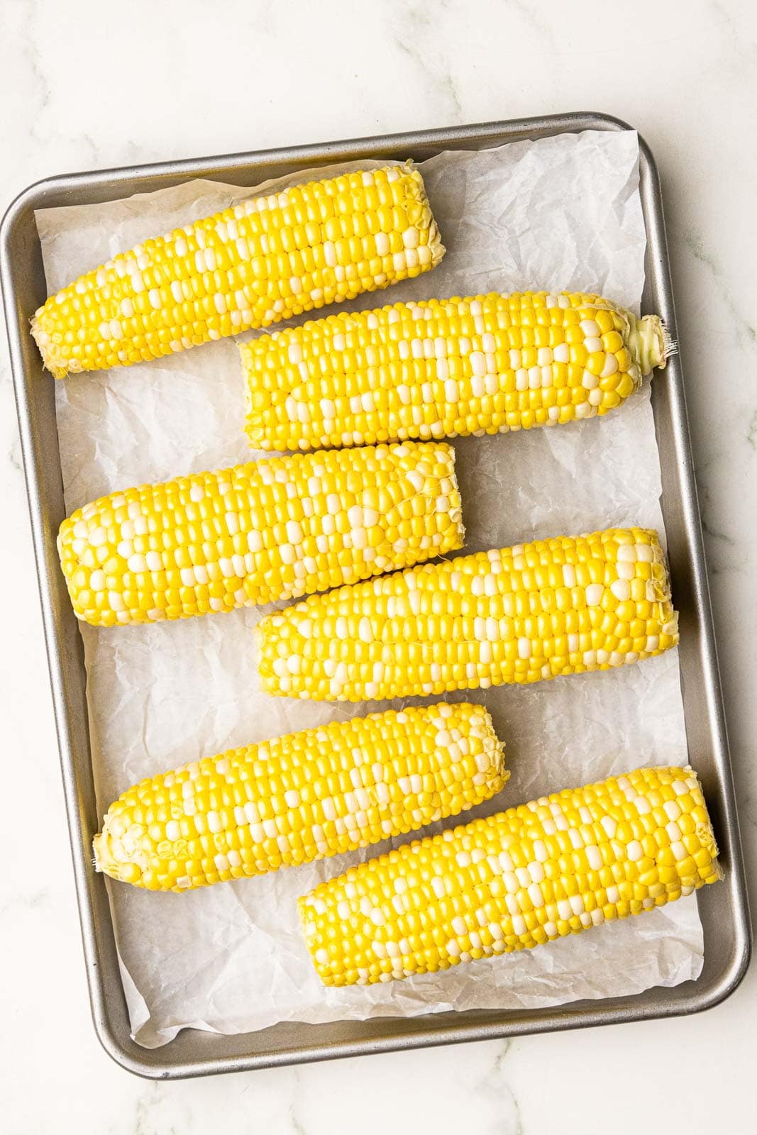 overhead view of six years of corn on parchment lined cooking sheet