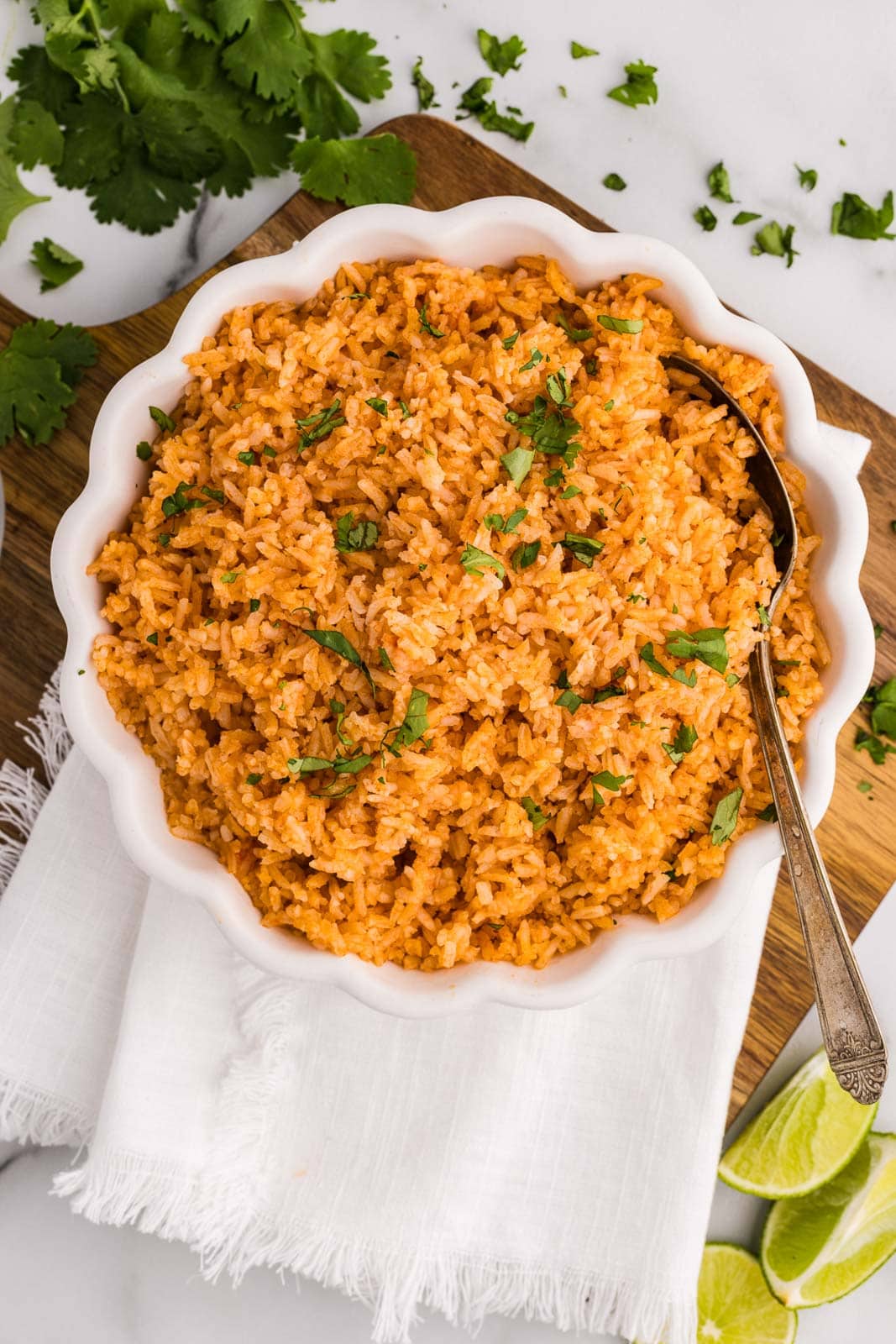overhead view of white bowl containing Spanish rice on white dishtowel on wooden cutting board