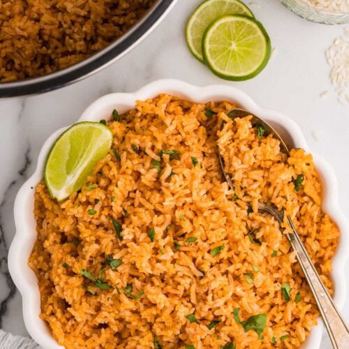 overhead view of white bowl containing Spanish rice with bowl of Spanish rice, two lime slices and jar of white rice in background