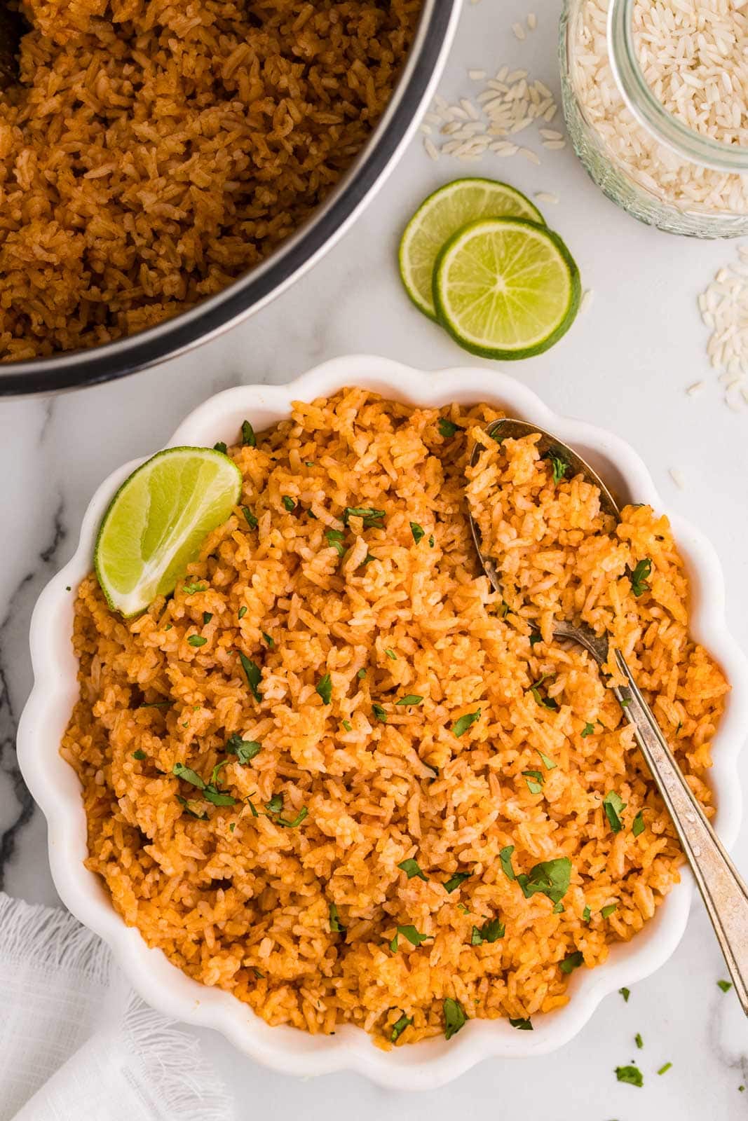 overhead view of white bowl containing Spanish rice with bowl of Spanish rice, two lime slices and jar of white rice in background