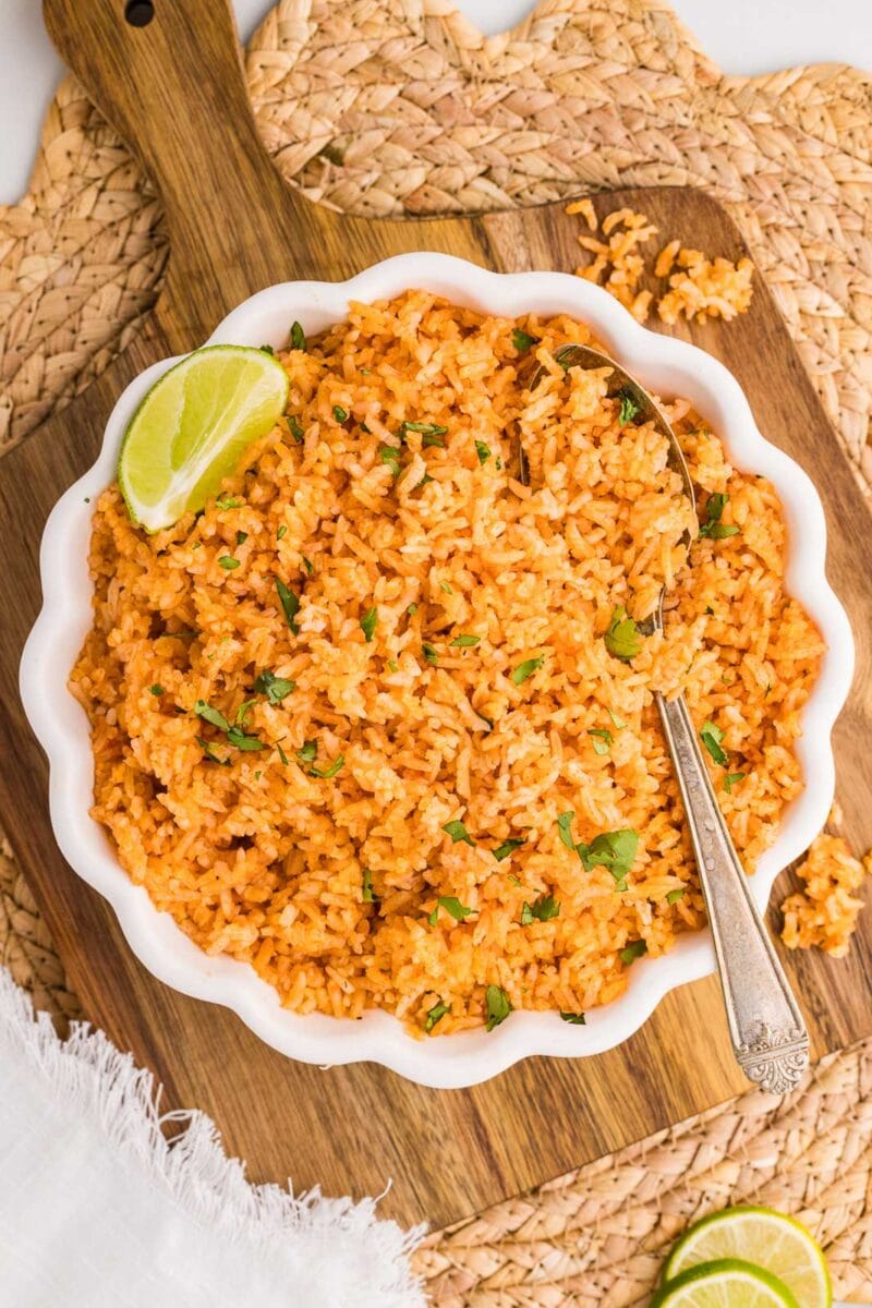 overhead view of white bowl of Spanish rice with spoon, on wooden cutting board and placemat