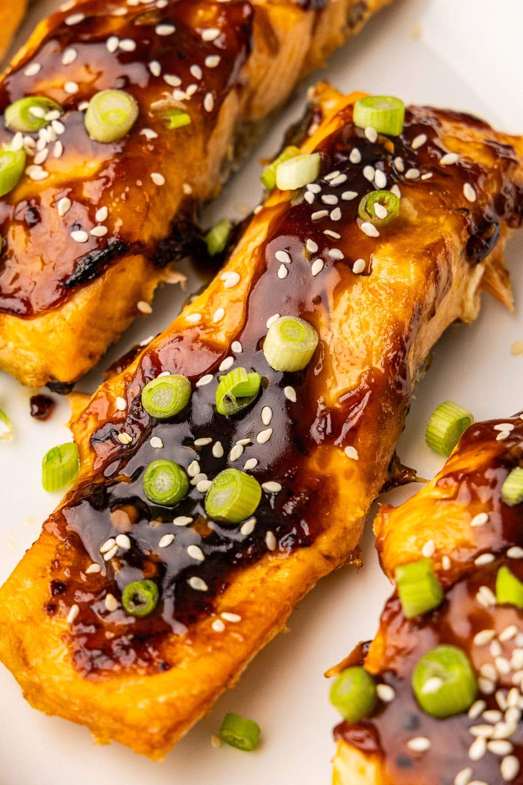 overhead closeup view of salmon fillets topped with green onions, sesame seeds, and chili garlic sauce