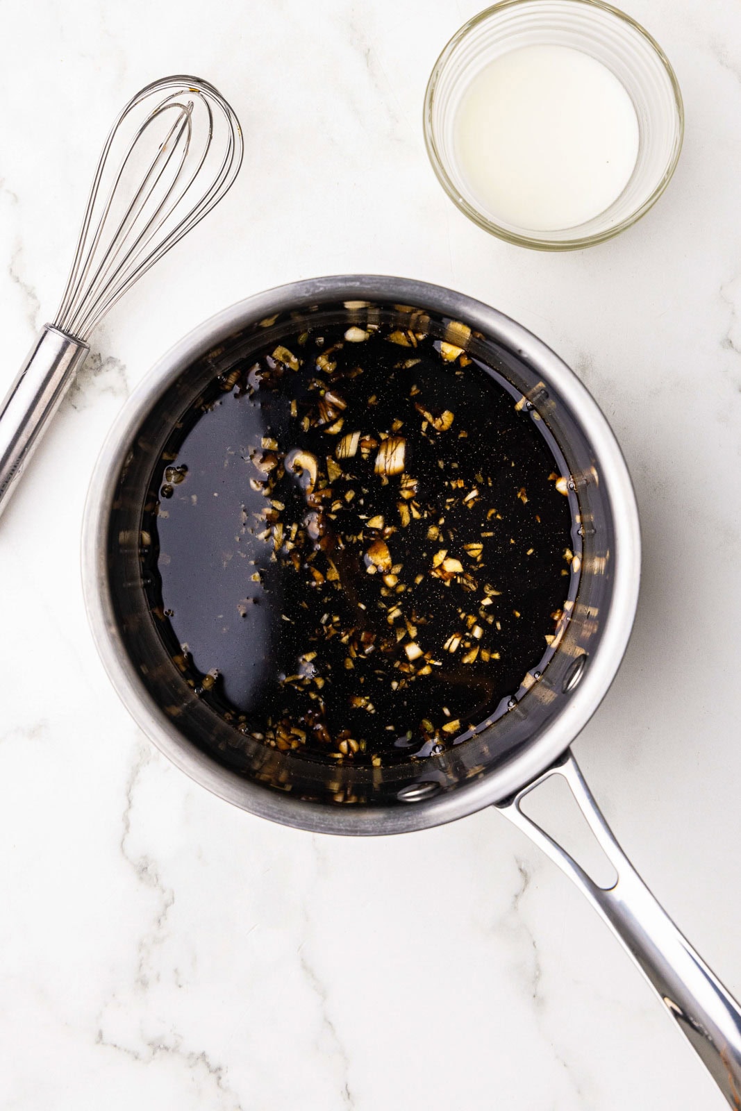 saucepan with mixture with whisk and cornstarch slurry on side