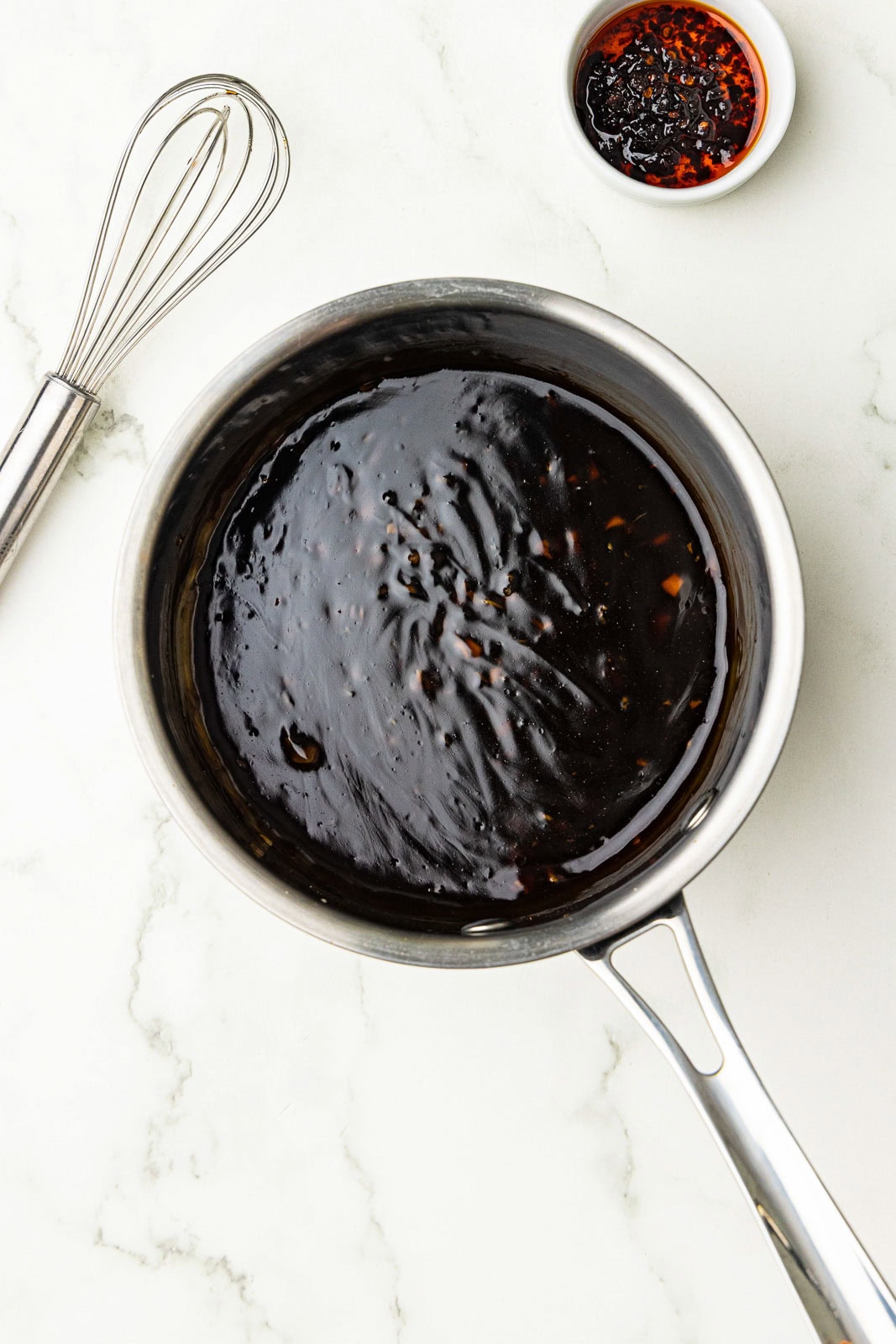 saucepan with mixture, whisk and chili garlic sauce on side