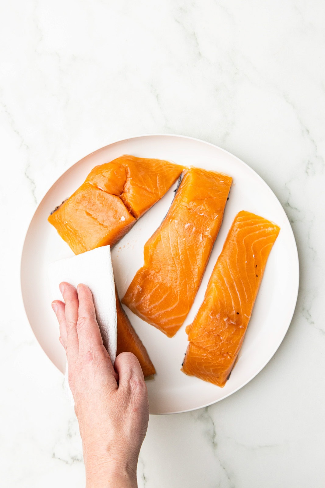 hand patting salmon fillets dry on white dinner plate