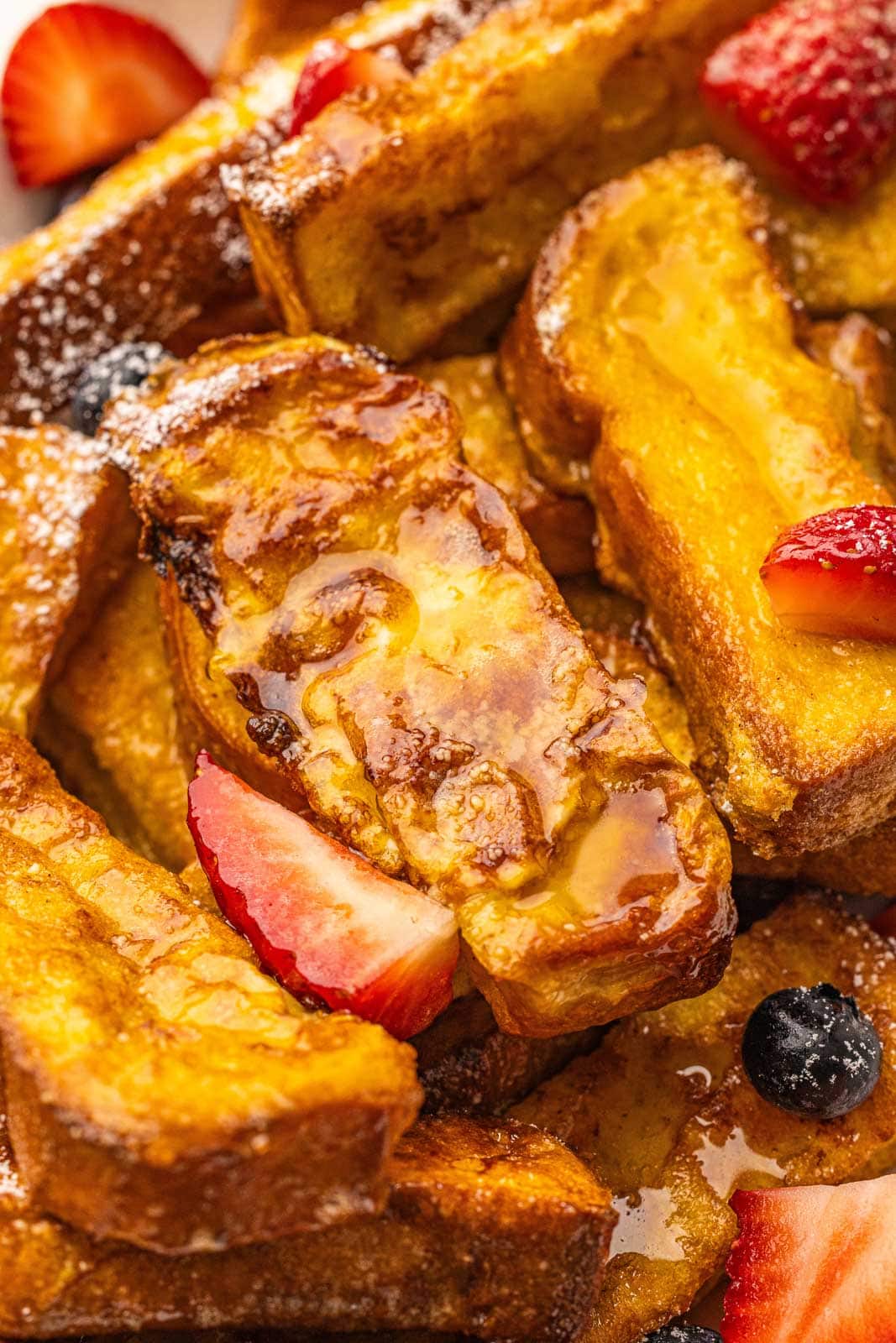 closeup view of french toast sticks and fruit, smothered in maple syrup