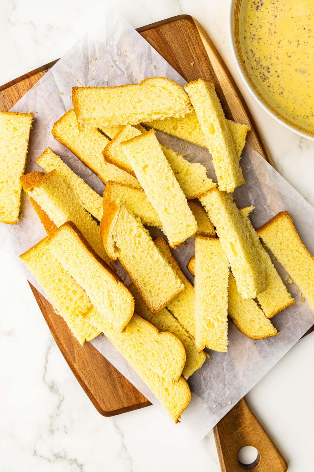 parchment paper lined wooden cutting board with sliced brioche and bowl of mixed ingredients on side
