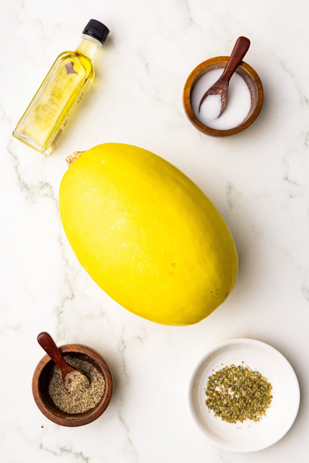 ingredients to include 1 spaghetti squash, olive oil, wooden bowls and spoons of salt and pepper, and white bowl of Italian seasoning