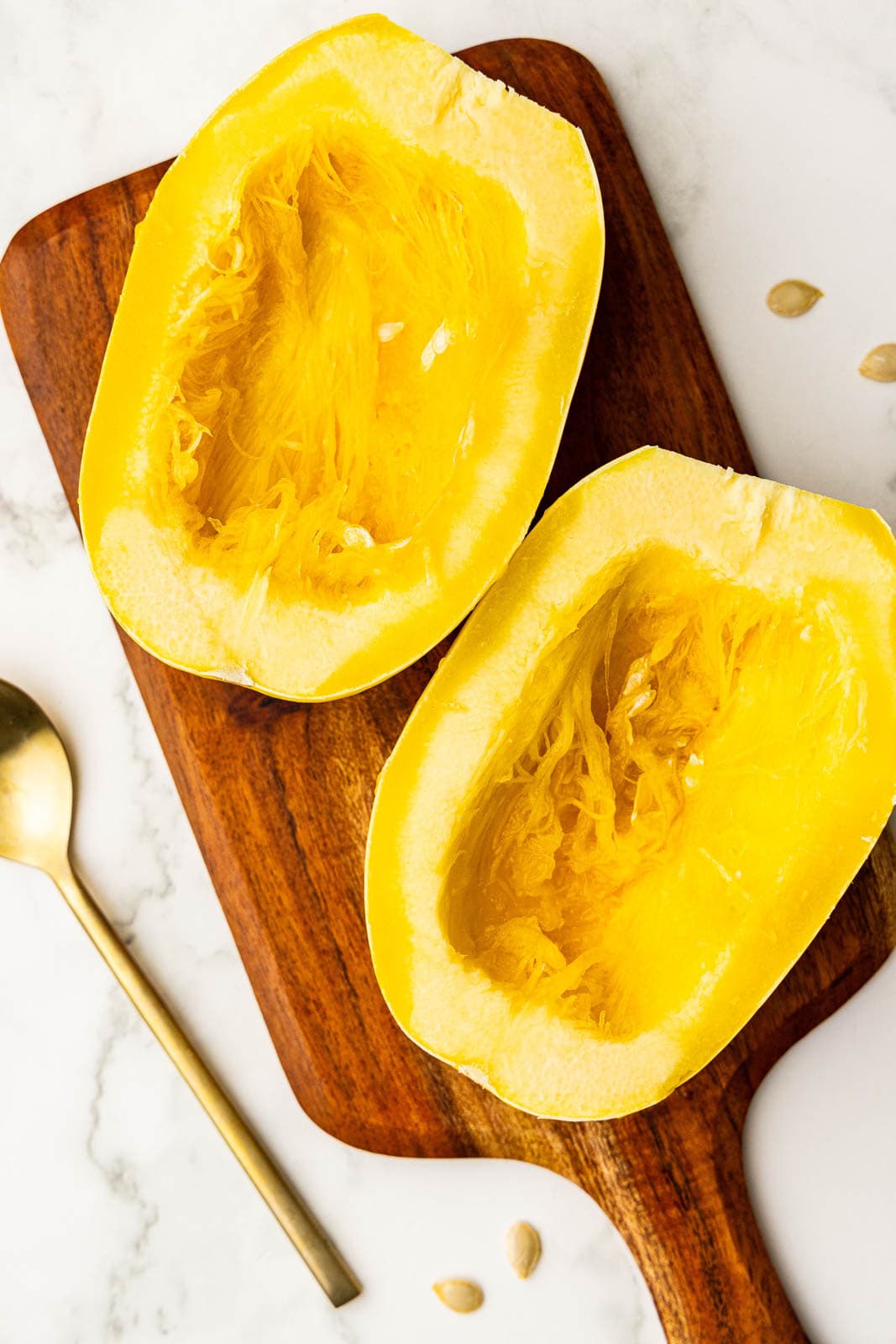 two halves of squash on wooden cutting board with seeds scooped out and spoon on side